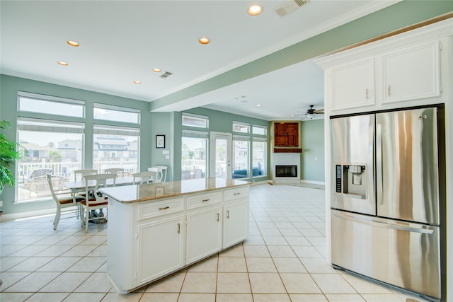 kitchen with light stone counters, a fireplace, light tile patterned floors, white cabinets, and stainless steel fridge with ice dispenser