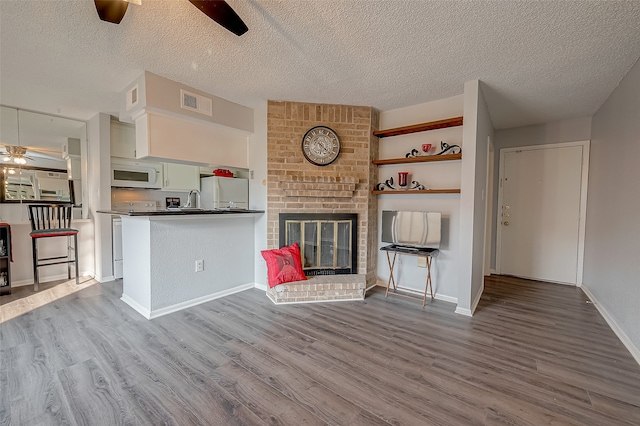 unfurnished living room featuring light hardwood / wood-style floors, a textured ceiling, a fireplace, and ceiling fan