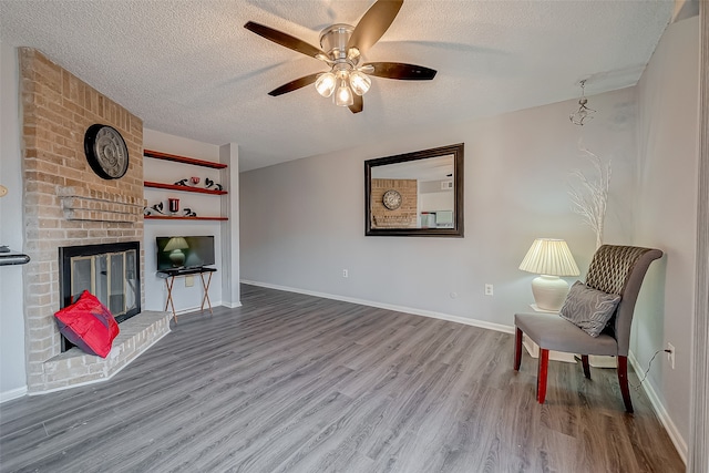 living area featuring a textured ceiling, hardwood / wood-style flooring, ceiling fan, and a brick fireplace