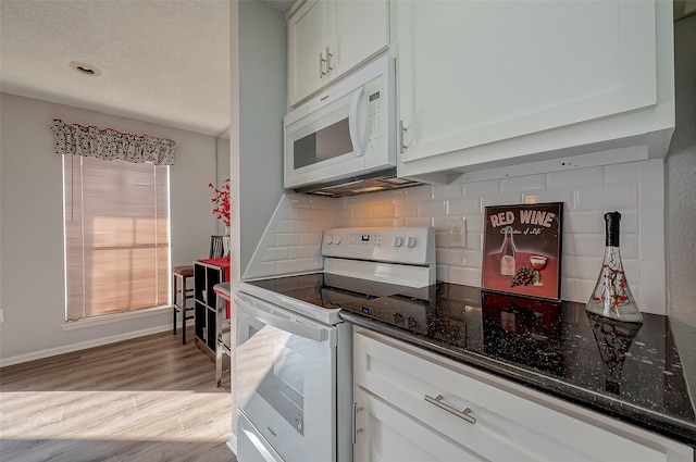 kitchen with tasteful backsplash, white cabinets, white appliances, light wood-type flooring, and dark stone counters