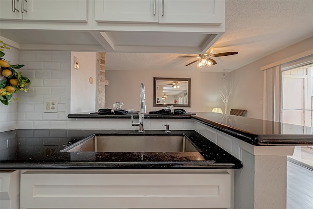 kitchen featuring white cabinets, backsplash, kitchen peninsula, and sink