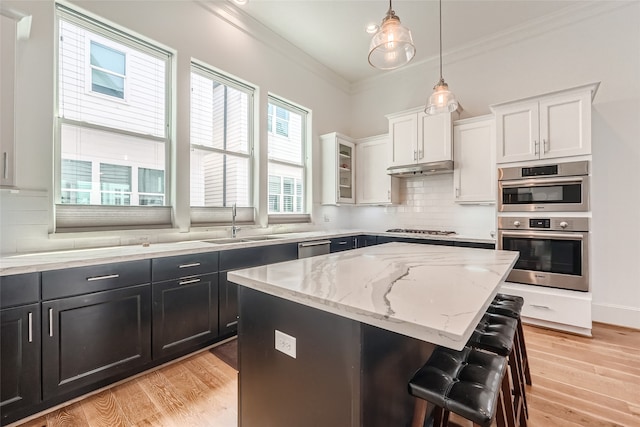 kitchen with ornamental molding, appliances with stainless steel finishes, decorative backsplash, and light wood-type flooring