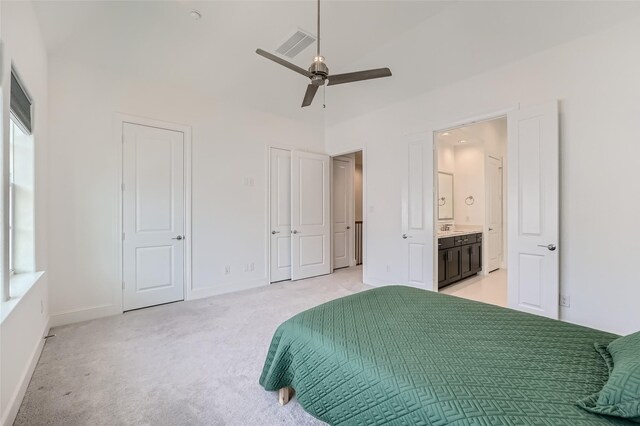 bedroom featuring multiple closets, ensuite bath, light carpet, and ceiling fan