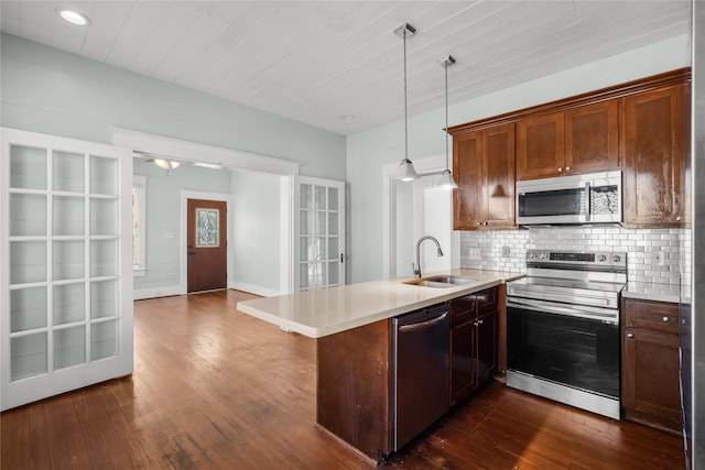 kitchen with dark hardwood / wood-style flooring, kitchen peninsula, sink, appliances with stainless steel finishes, and decorative light fixtures