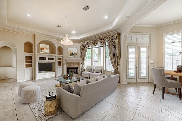 living room with a tiled fireplace, crown molding, a chandelier, a raised ceiling, and built in features