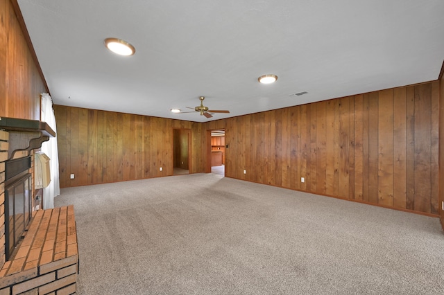 unfurnished living room featuring wooden walls, a fireplace, ceiling fan, and light colored carpet