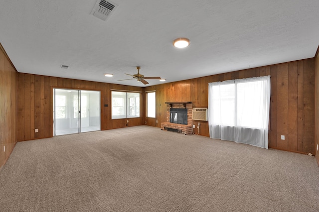 unfurnished living room featuring wood walls, a wall mounted air conditioner, ceiling fan, a fireplace, and carpet