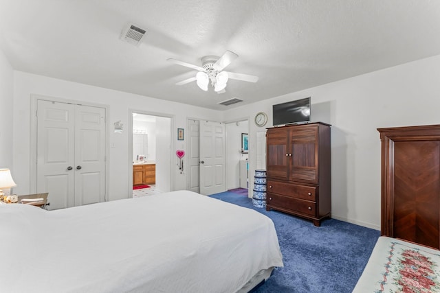 bedroom featuring a ceiling fan, visible vents, dark carpet, and ensuite bathroom