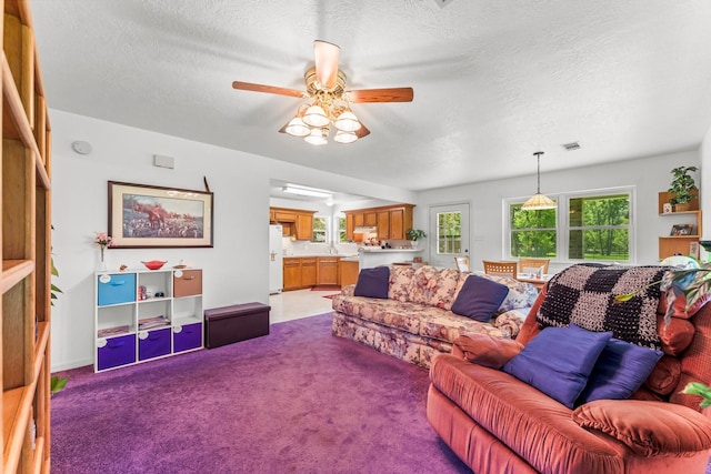 living room featuring a textured ceiling, carpet flooring, visible vents, and a ceiling fan