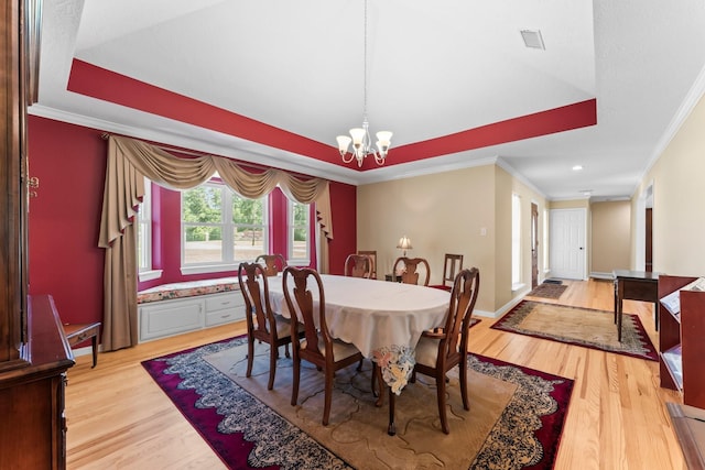 dining room with a chandelier, a tray ceiling, crown molding, and light wood-style floors