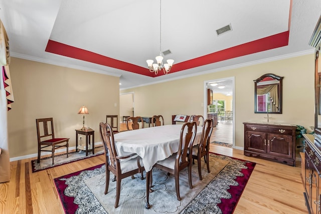 dining room featuring a tray ceiling, visible vents, light wood finished floors, and an inviting chandelier