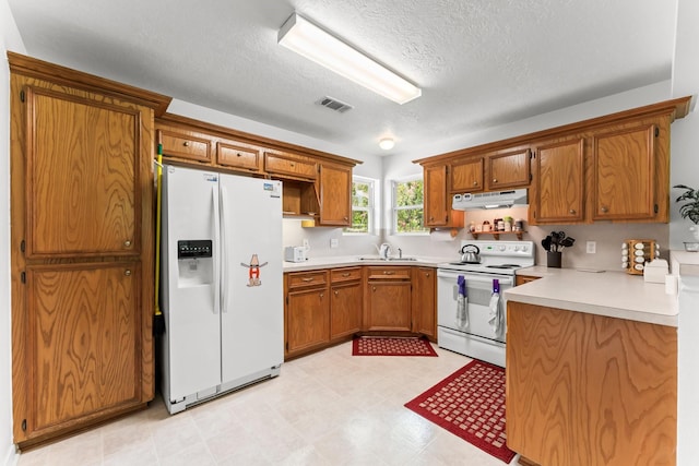 kitchen featuring visible vents, brown cabinetry, a sink, white appliances, and under cabinet range hood