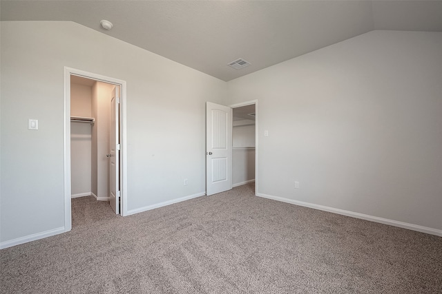 unfurnished bedroom featuring carpet flooring, vaulted ceiling, a closet, and a walk in closet