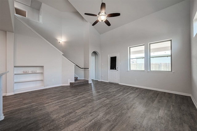 unfurnished living room featuring built in shelves, a high ceiling, ceiling fan, and dark wood-type flooring