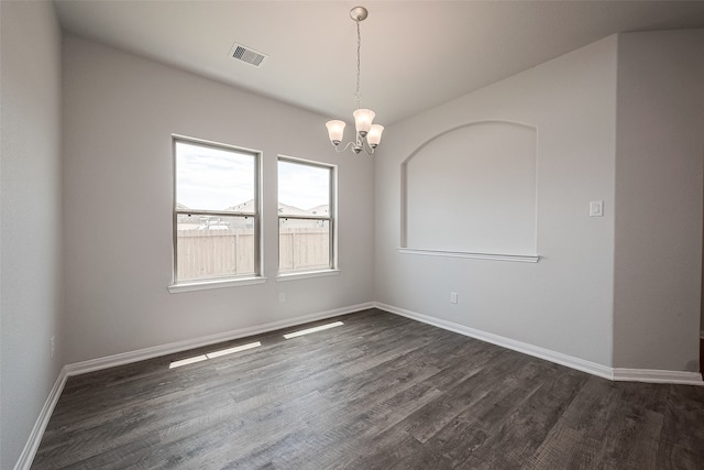 empty room with dark wood-type flooring and an inviting chandelier