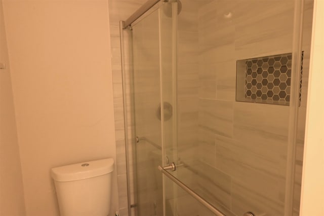 bathroom with a shower with shower door and toilet