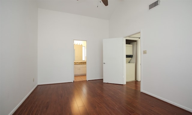 unfurnished bedroom with ensuite bath, ceiling fan, dark hardwood / wood-style flooring, and a towering ceiling