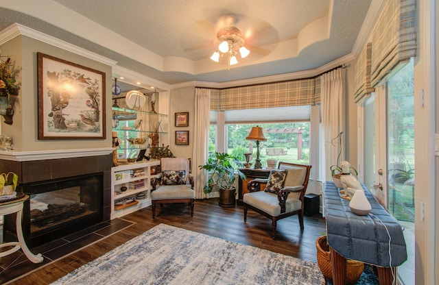 sitting room with a tile fireplace, ceiling fan, a raised ceiling, dark hardwood / wood-style flooring, and ornamental molding