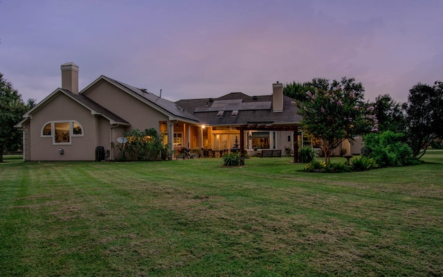 back house at dusk featuring solar panels and a lawn