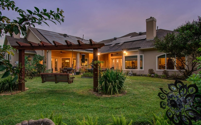 back house at dusk with solar panels, an outdoor hangout area, ceiling fan, and a lawn