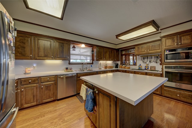 kitchen with appliances with stainless steel finishes, light wood-type flooring, ornamental molding, sink, and a center island