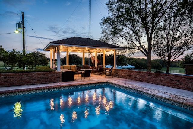 pool at dusk featuring a gazebo, a patio, and an outdoor hangout area