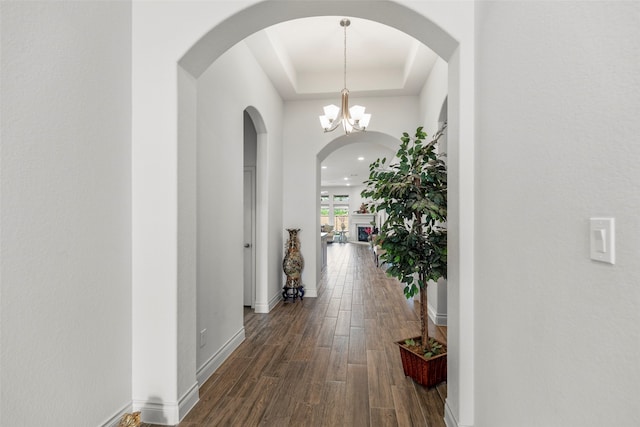 hallway with an inviting chandelier, dark hardwood / wood-style floors, and a tray ceiling