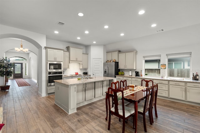 kitchen with tasteful backsplash, stainless steel appliances, a center island with sink, hardwood / wood-style floors, and light stone counters