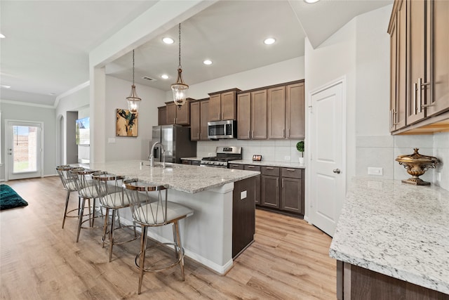 kitchen with a kitchen island with sink, stainless steel appliances, light hardwood / wood-style floors, decorative backsplash, and decorative light fixtures