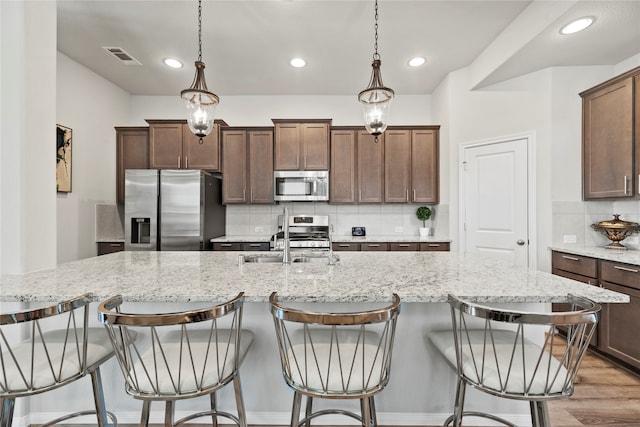 kitchen featuring stainless steel appliances, decorative light fixtures, tasteful backsplash, and light wood-type flooring