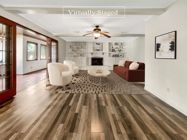 living room featuring built in shelves, beam ceiling, wood-type flooring, and ceiling fan