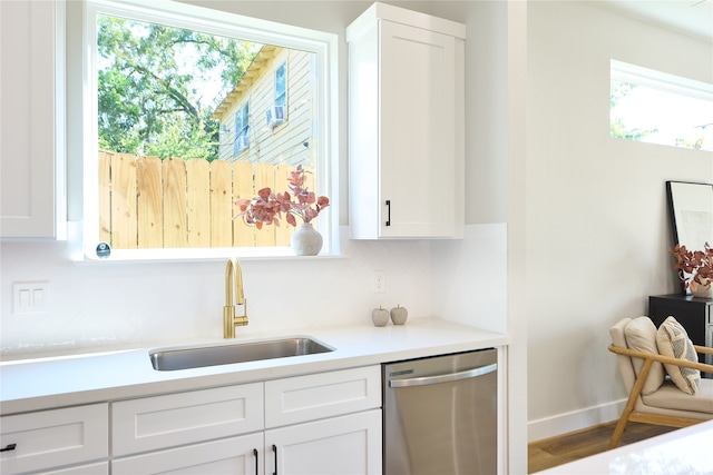 kitchen with hardwood / wood-style floors, white cabinets, stainless steel dishwasher, and sink