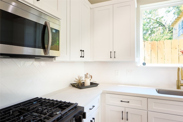 kitchen featuring black range with gas stovetop, white cabinetry, and sink