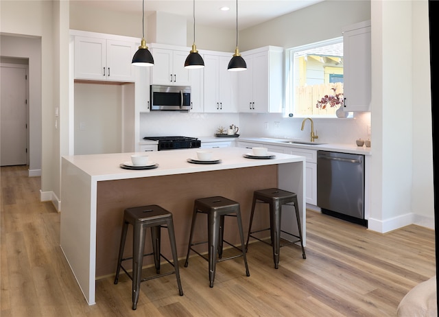 kitchen featuring white cabinets, stainless steel appliances, decorative light fixtures, and a kitchen island