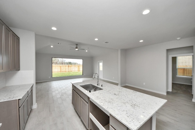 kitchen featuring ceiling fan, sink, light stone counters, light hardwood / wood-style floors, and a kitchen island with sink