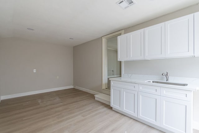 kitchen with light stone counters, sink, light wood-type flooring, and white cabinetry