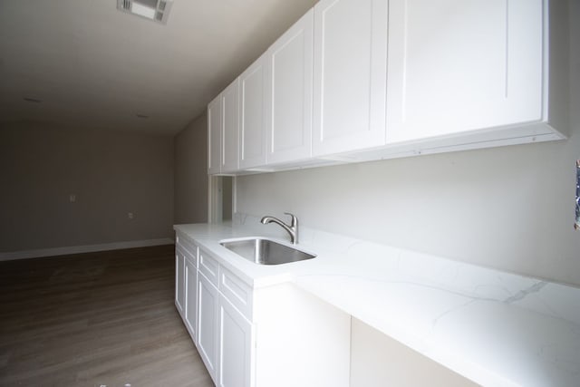 kitchen featuring white cabinets, wood-type flooring, light stone counters, and sink