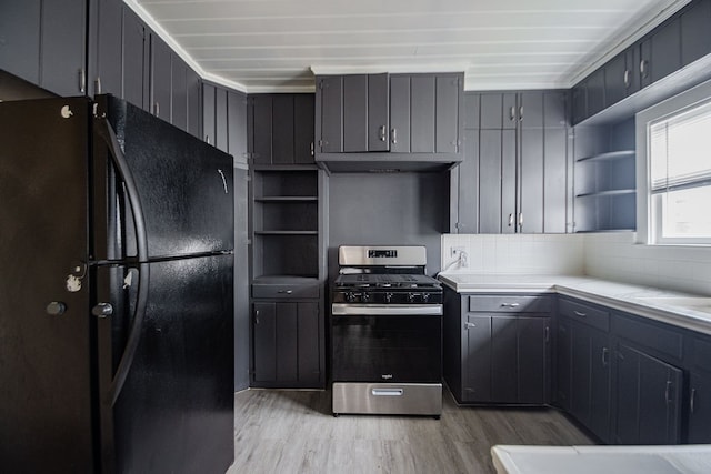 kitchen featuring stainless steel gas range oven, light hardwood / wood-style flooring, gray cabinets, decorative backsplash, and black refrigerator