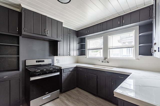 kitchen with light wood-type flooring, backsplash, stainless steel range with gas cooktop, and sink