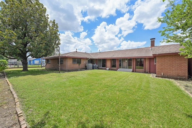 back of house with central AC unit, a sunroom, and a lawn