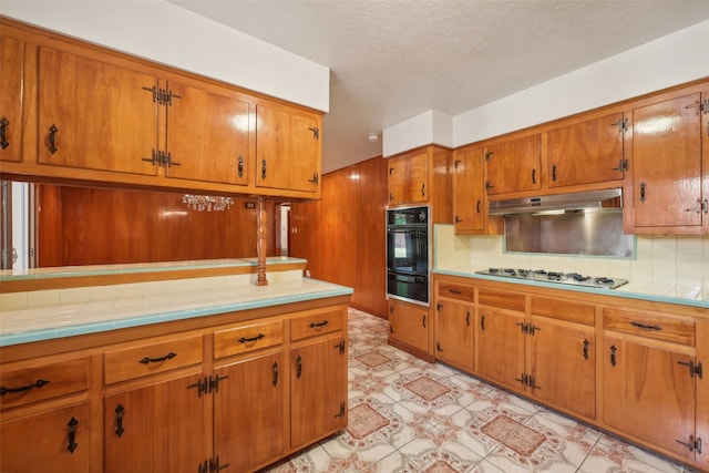 kitchen with decorative backsplash, tile counters, white gas cooktop, oven, and a textured ceiling