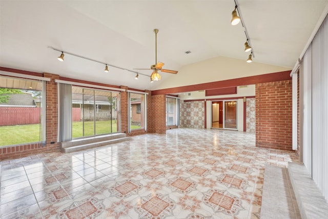 unfurnished living room with lofted ceiling, track lighting, ceiling fan, light tile patterned flooring, and brick wall