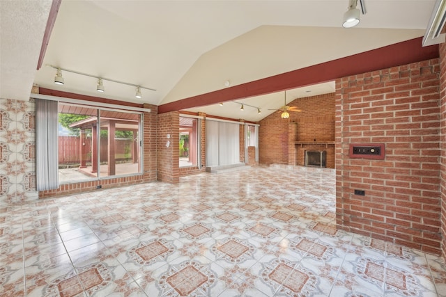 unfurnished living room featuring a brick fireplace, rail lighting, ceiling fan, vaulted ceiling, and brick wall