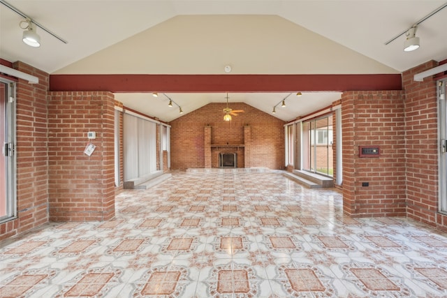 unfurnished living room featuring track lighting, brick wall, a fireplace, and vaulted ceiling