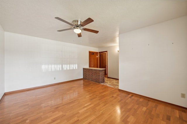 empty room featuring light hardwood / wood-style flooring, a fireplace, a textured ceiling, and ceiling fan