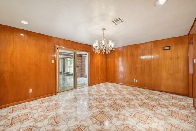 spare room with a chandelier and wood walls