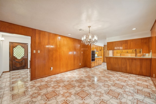 unfurnished living room featuring a chandelier and wood walls