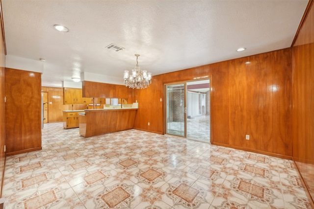 kitchen with kitchen peninsula, a textured ceiling, wooden walls, and a notable chandelier