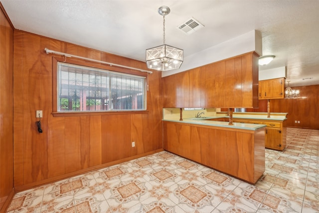 kitchen featuring wood walls, a textured ceiling, kitchen peninsula, pendant lighting, and a notable chandelier