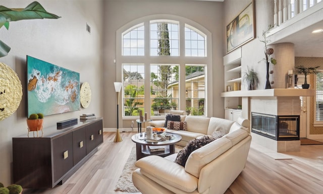 living room with a towering ceiling, light wood-type flooring, and a tile fireplace